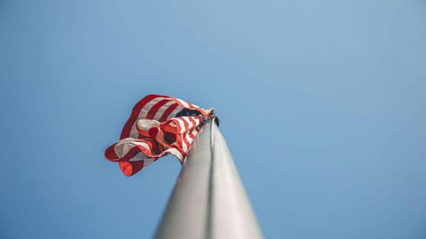 Looking up at an American flag on a silver pole with blue sky background